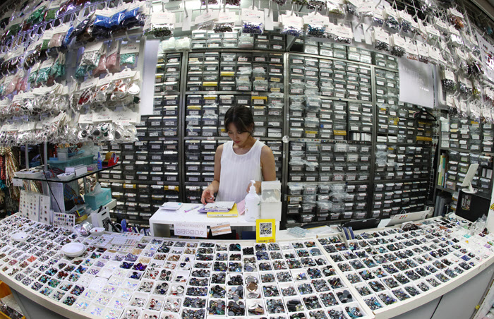 Woman organizing handmade jewelry components at Namdaemun Market stall in Seoul