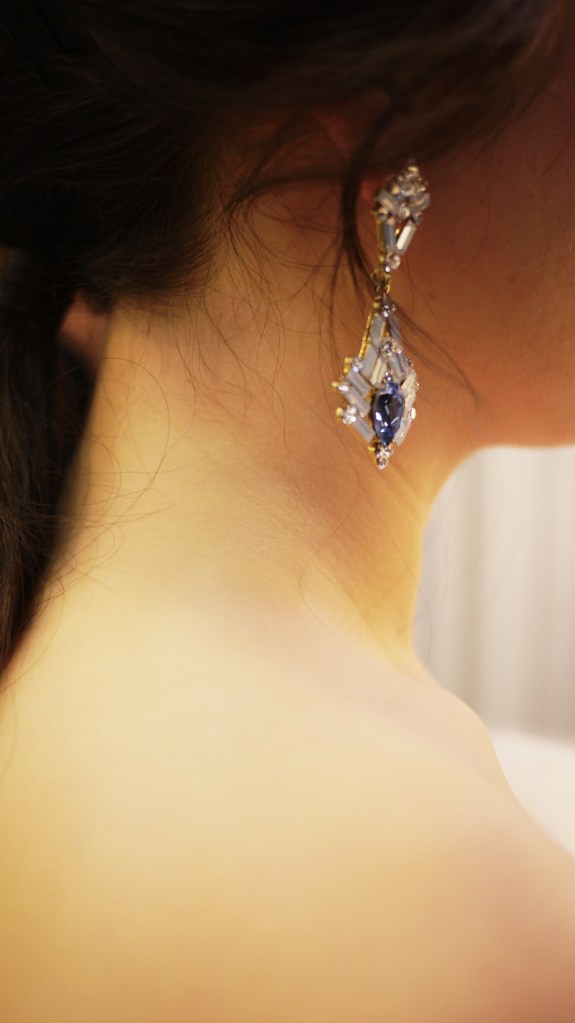 Close-up of a woman's neck and earrings featuring intricate designs with a large central stone, showcasing elegance and craftsmanship.