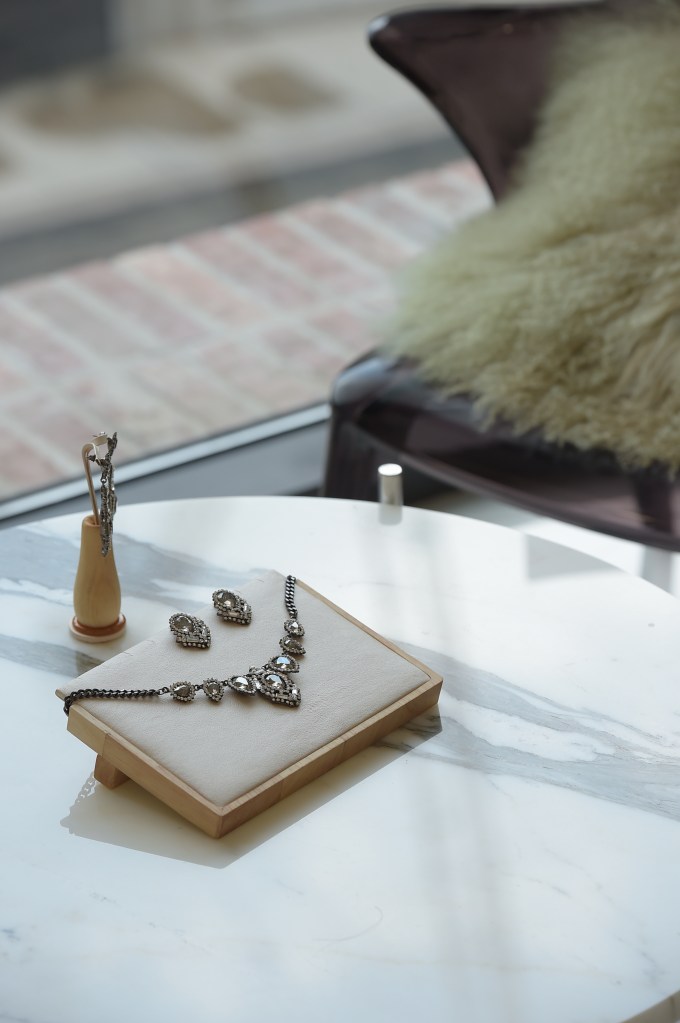 A delicate necklace and matching earrings from the Smoky Gray Collection, elegantly displayed on a soft fabric tray atop a marble table, with natural light filtering through, highlighting the pieces' intricate craftsmanship.