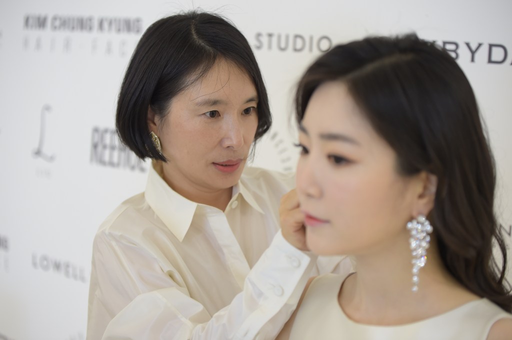 A stylist carefully adjusts the earring of a bride during a wedding preparation, with a focus on the intricate details of bridal fashion.