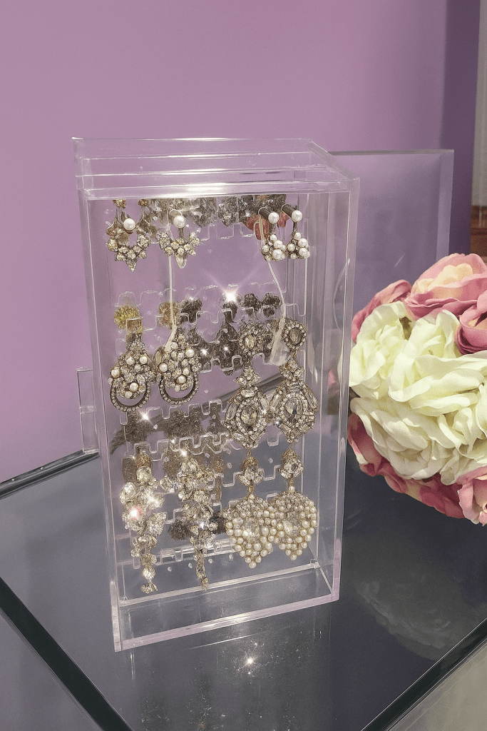 A display case featuring various elegant handmade earrings, showcasing intricate designs with crystals and pearls, set against a pastel purple background.